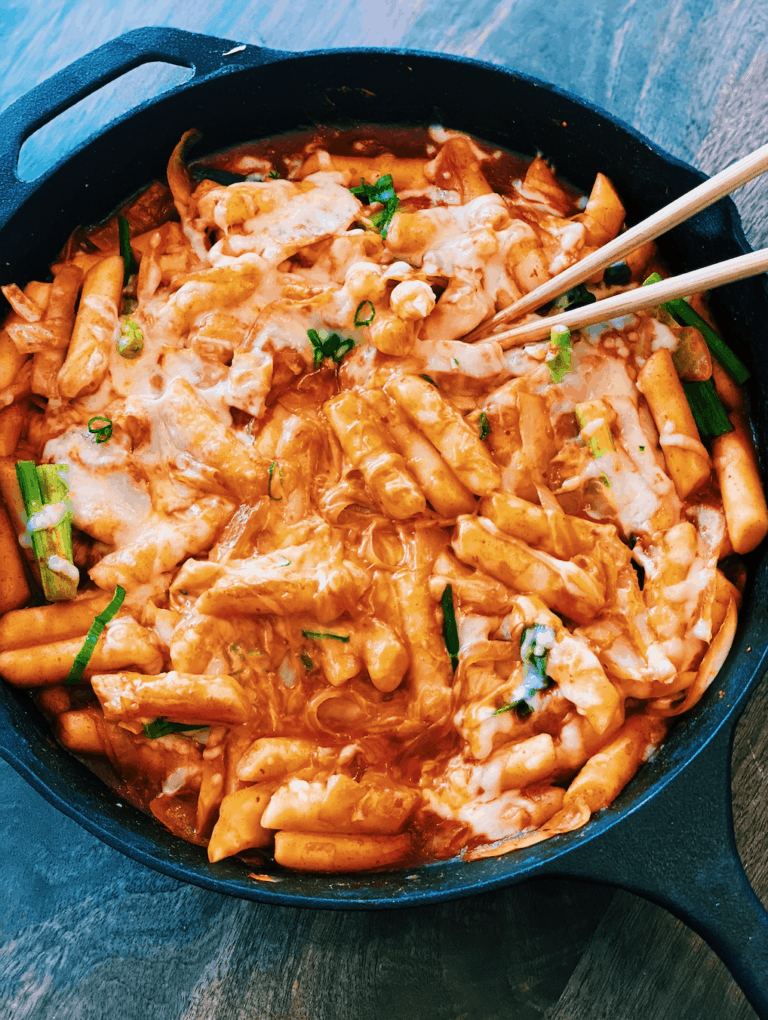 Scrumptious Spicy & Cheesy Korean Rice Cakes (Tteokbokki) topped with gooey melted cheese. This image features chewy rice cakes coated in a vibrant, spicy sauce, creating a visually appealing and mouth-watering dish. Perfect for food lovers who enjoy a fusion of spicy, savory, and cheesy flavors in a traditional Korean street food favorite.