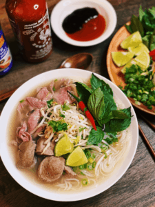 A Bowl Of Instant Pot Beef Pho with sliced sirloin, meatballs garnished with Thai chili, fresh Thai basil, bean sprouts, and lime wedges