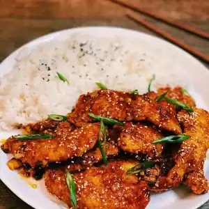 Spicy Honey Garlic Chicken Tenders Served on a Plate of White Rice garnished with sesame seeds and green onions