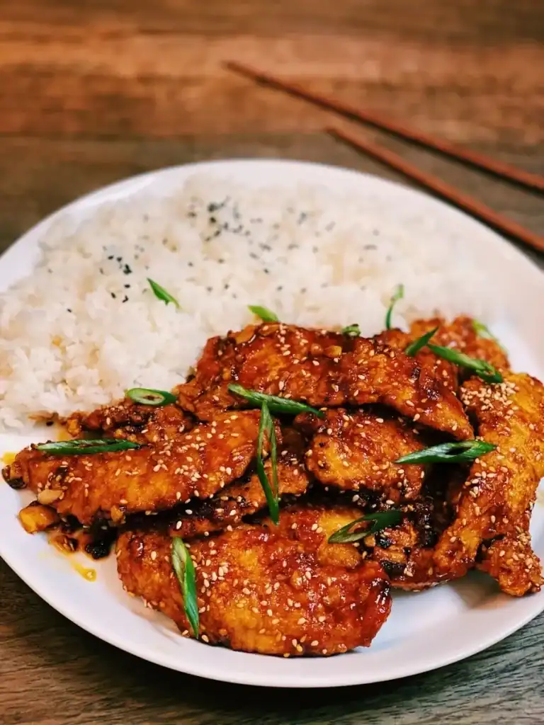 Spicy Honey Garlic Chicken Tenders Served on a Plate of White Rice garnished with sesame seeds and green onions