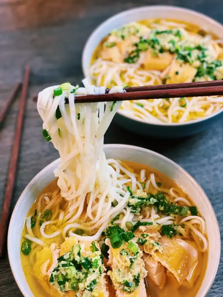 Picking up noodles with chopsticks in a bowl of Asian Inspired Hainan Chicken Noodle Soup