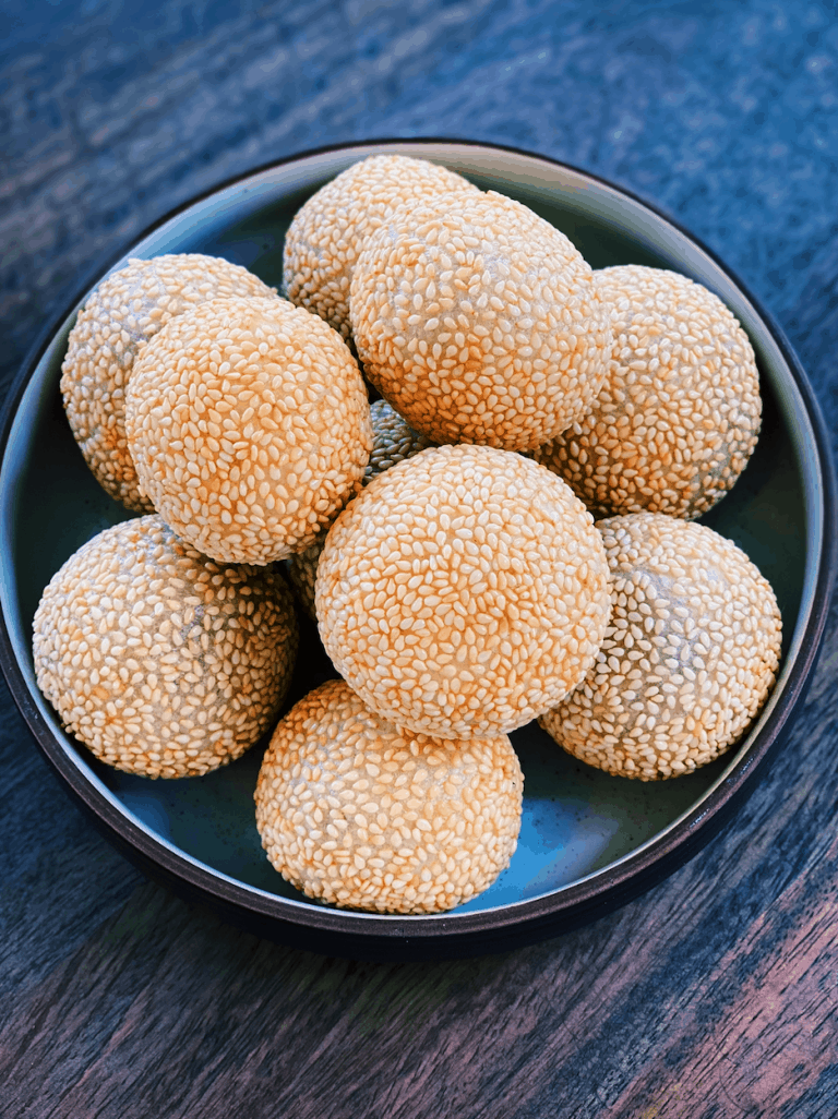 A picture of golden, deep-fried Sesame Balls, a traditional Asian dessert, crispy on the outside with a chewy interior, served at a Christmas gathering.