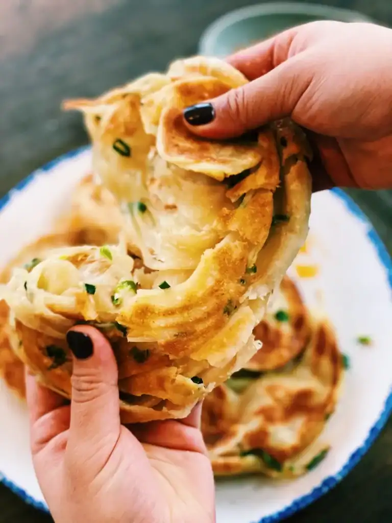 Tearing a scallion pancake in half to show flaky layers