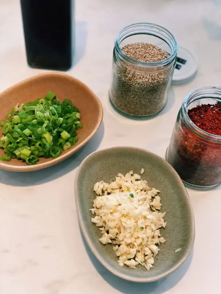 Seasoning for Korean Beansprout Side Dish including chili powder, sesame seeds, minced garlic, chopped green onion, and sesame oil