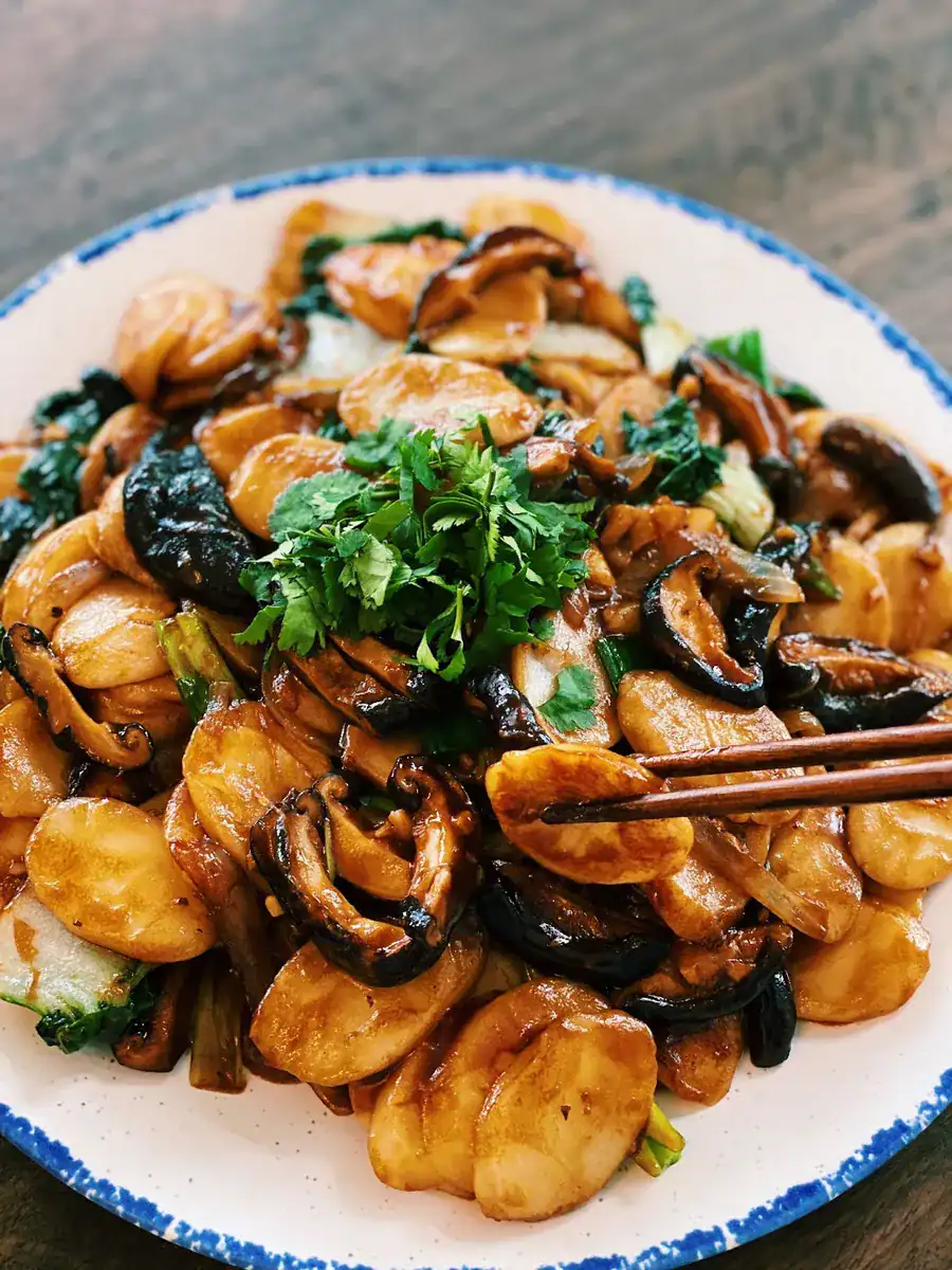 A plate of Shanghai Stir Fried Rice Cakes with a piece of rice cake picked up by chopsticks