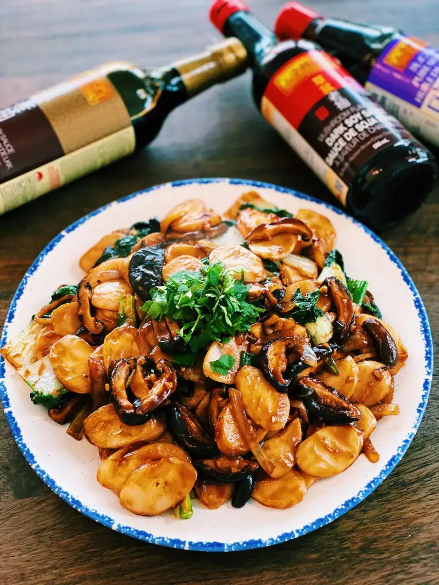 A plate of Shanghai Stir Fried Rice Cakes with bottles of soy sauce, dark soy sauce, and oyster sauce around