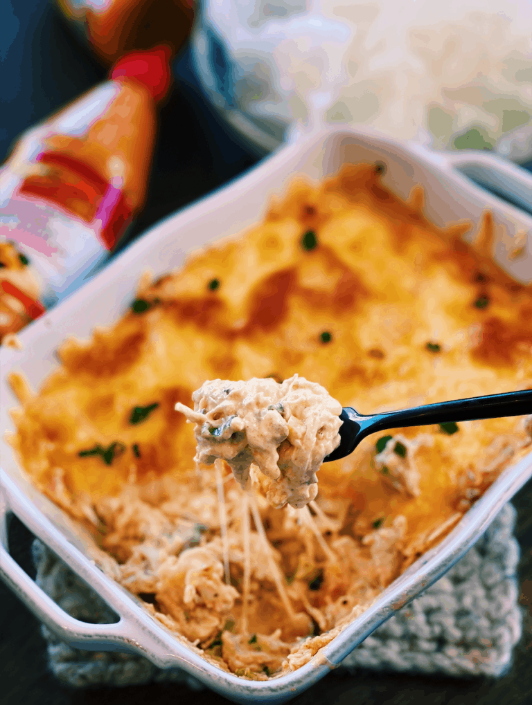 A freshly baked dish of Sriracha Mayo Chicken Dip, with a spoonful lifted to show texture
