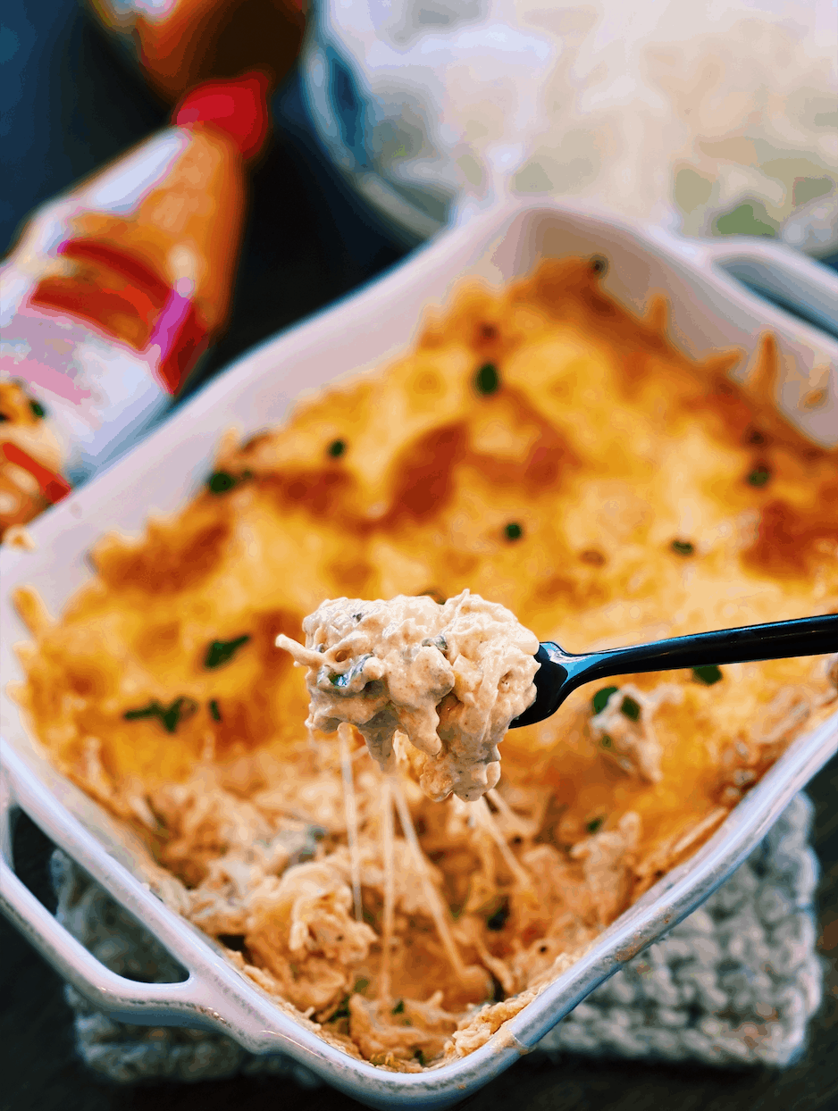 A freshly baked dish of Sriracha Mayo Chicken Dip, with a spoonful lifted to show texture