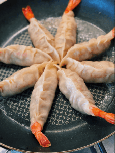 Pan Frying Whole Shrimp Potstickers arranged in a circle in the pan with the tails sticking towards the side of the pan