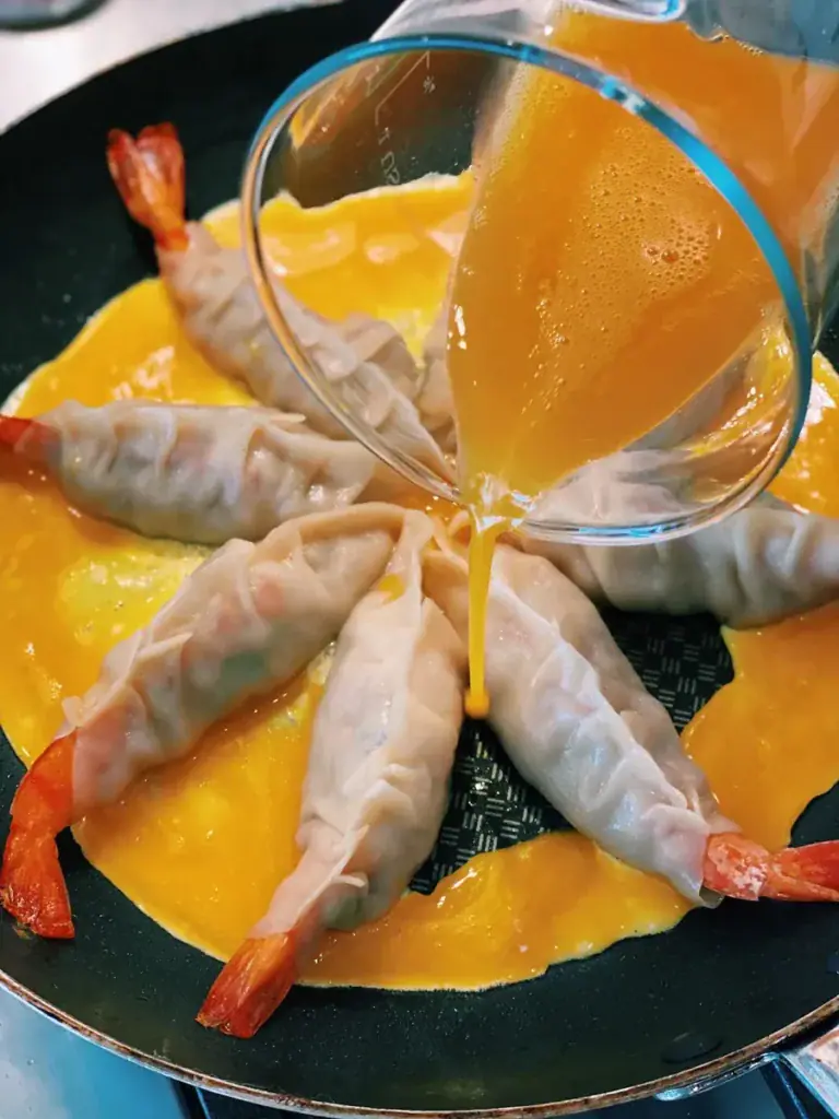 Pouring egg into empty spaces between dumplings for Egg Skirt Whole Shrimp Potstickers
