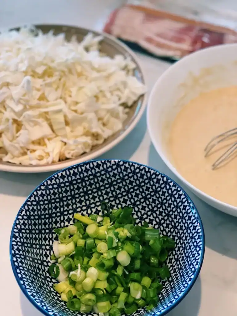 Okonomiyaki ingredients including batter, green onions, and sliced cabbage
