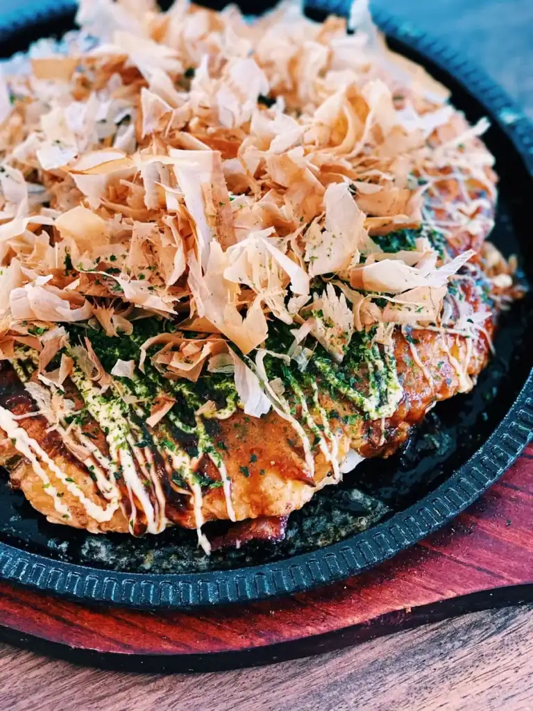 Okonomiyaki toppings including bonito flakes, Japanese mayo, takoyaki sauce, and seaweed powder