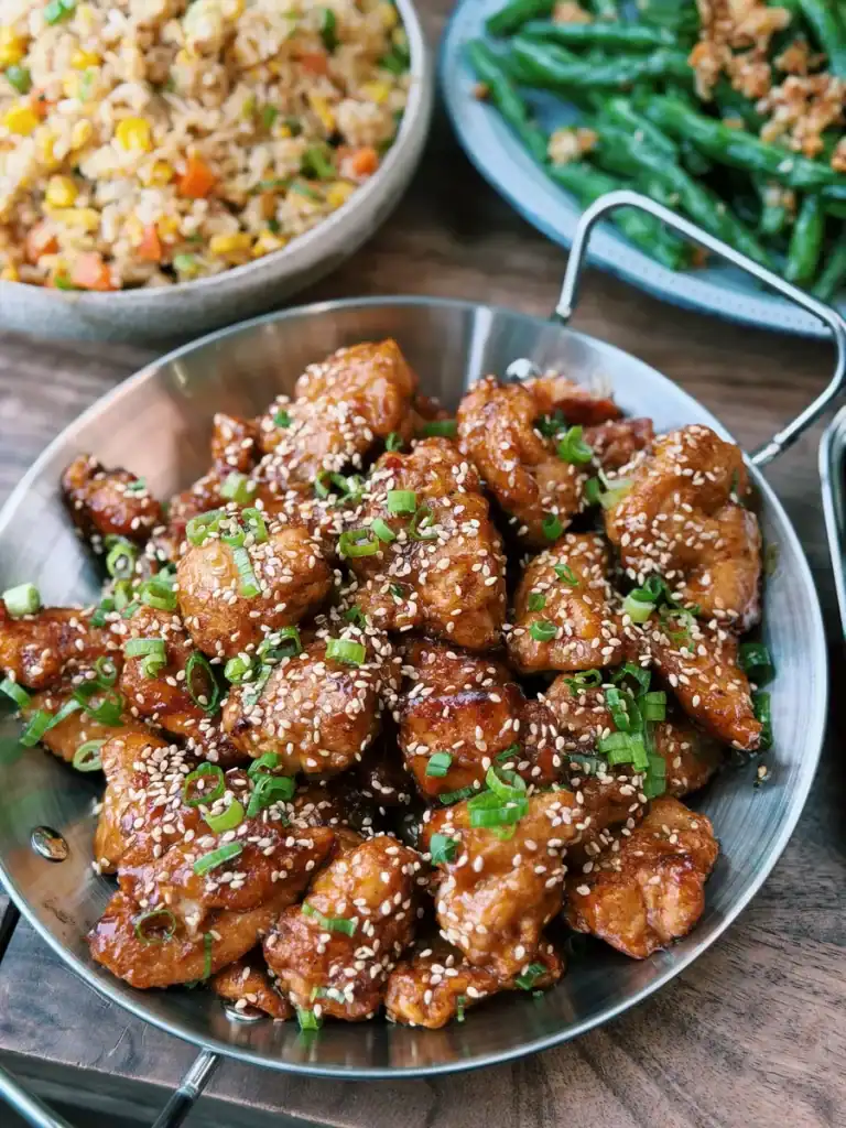 A plate full of orange chicken served with fried rice and garlic green beans