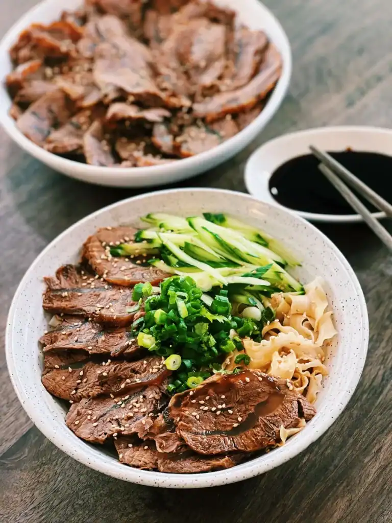Taiwanese Braised Beef Shanks Served Sliced on a bowl of noodles as a topping with a plate of sliced beef shank in the background