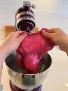 stretching pink beetroot dough for the window test for dough readiness for Beetroot Milk Bread