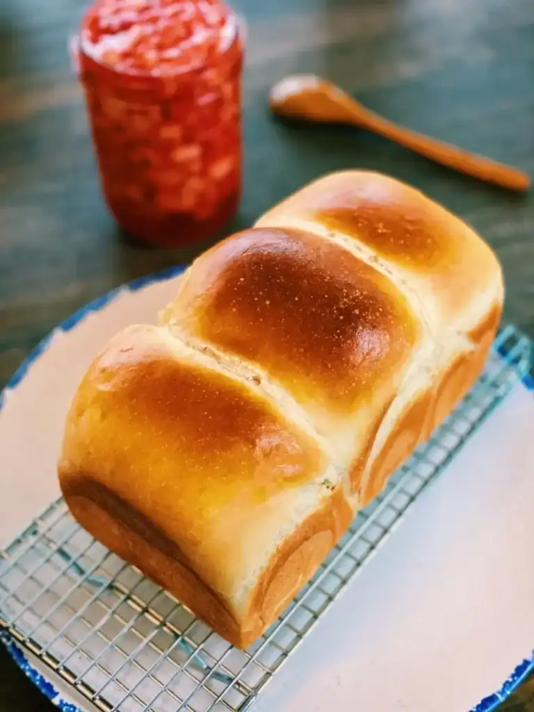 A loaf of freshly baked Beetroot Milk Bread, with a jar of homemade strawberry jam in the background