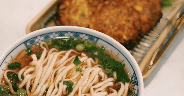 Delicious bowl of hot steaming noodles soup accompanied by savory vegetable pancakes. Great for a low, energy period day. Add a little spice to satisfy your spicy cravings. This appetizing Asian cuisine features perfectly cooked noodles immersed in a flavorful broth, garnished with vibrant vegetables and served alongside golden brown vegetable pancakes.