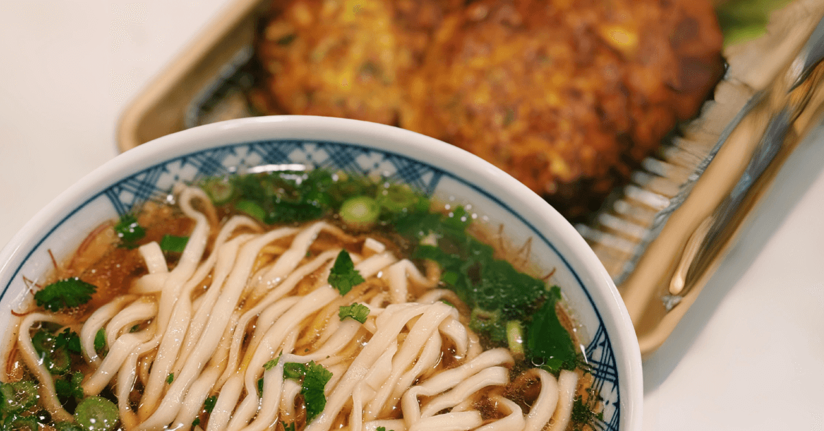 Delicious bowl of hot steaming noodles soup accompanied by savory vegetable pancakes. Great for a low, energy period day. Add a little spice to satisfy your spicy cravings. This appetizing Asian cuisine features perfectly cooked noodles immersed in a flavorful broth, garnished with vibrant vegetables and served alongside golden brown vegetable pancakes.