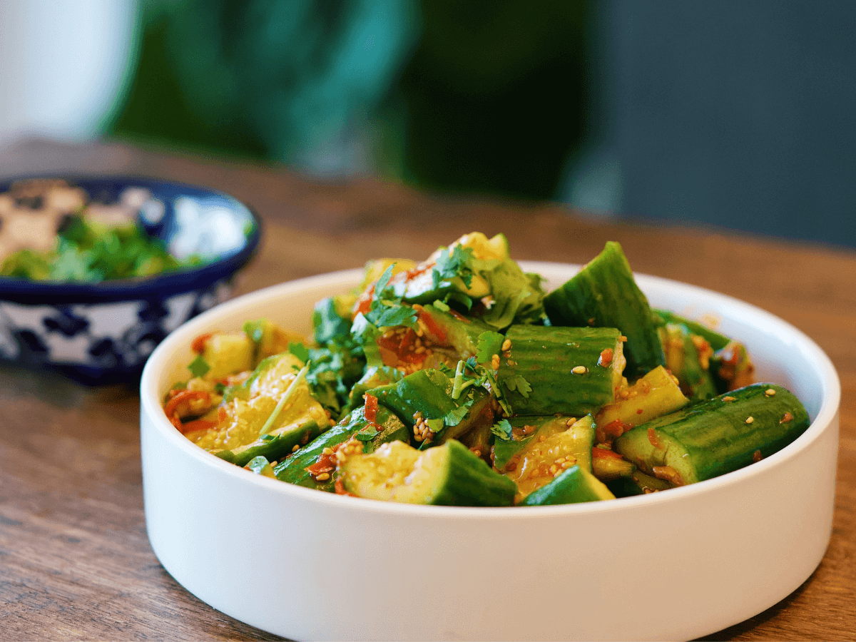 A vibrant bowl of spicy cucumber salad, a staple in Taiwanese cuisine, served on a wooden table. The fresh cucumber sticks are tossed with a spicy and tangy dressing, sprinkled with sesame seeds, and garnished with chopped cilantro, creating a dish that's as visually appealing as it is flavorful. The focus on the bright green of the cucumbers and the red flecks of chili makes this image perfect for articles on healthy eating, recipe blogs, or content highlighting traditional Asian salads.