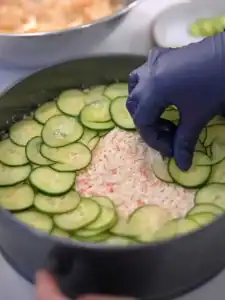 Adding a layer of cucumbers to the middle of Mayo Crab Spicy Salmon Sushi Cake