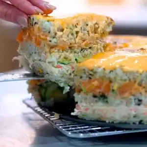 Slicing a Mayo Crab Spicy Salmon Sushi Cake to reveal the layers of rice, spicy salmon, and mayo crab