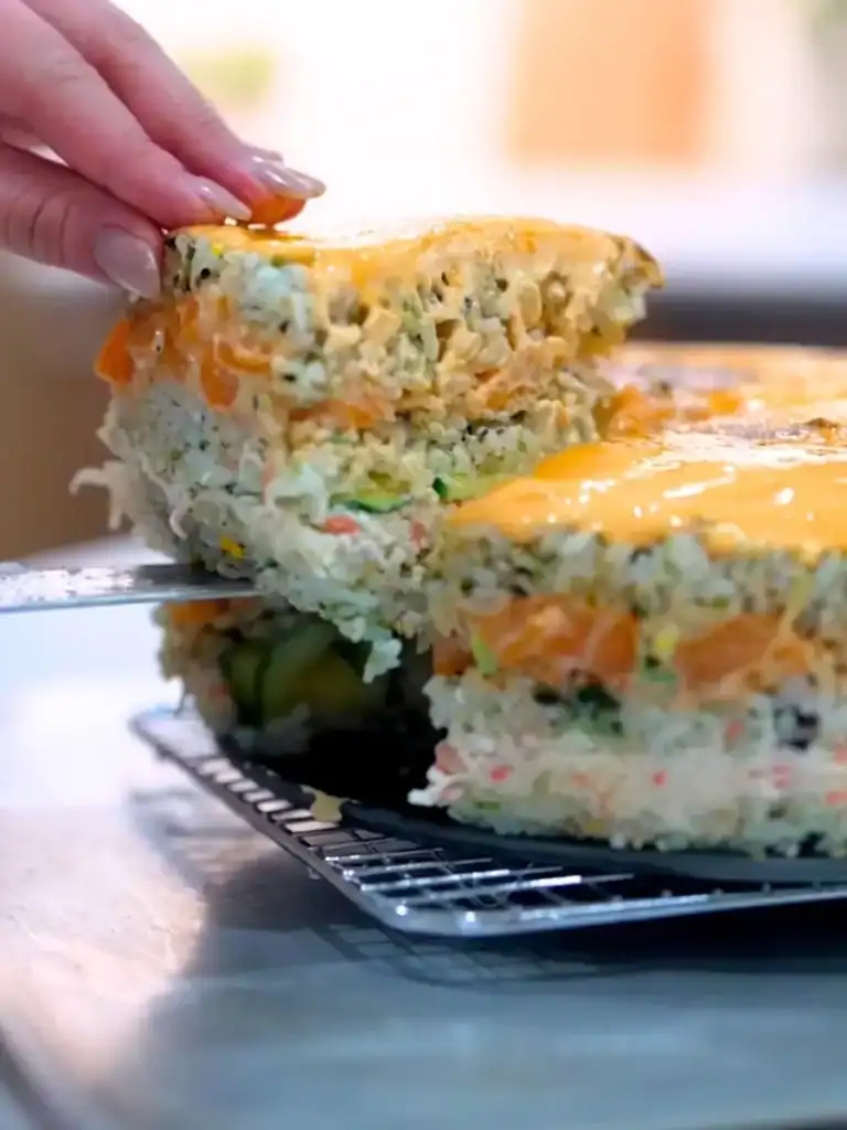 Slicing a Mayo Crab Spicy Salmon Sushi Cake to reveal the layers of rice, spicy salmon, and mayo crab