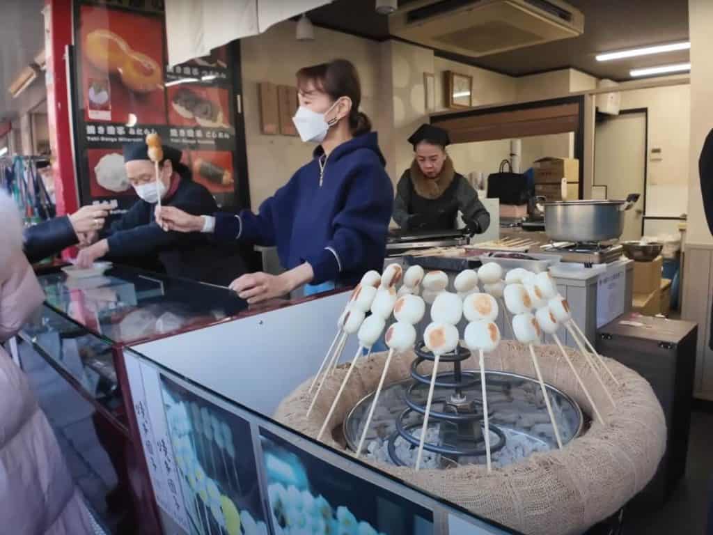 Shopkeepers selling grilled rice cakes, with a circle of rice cake skewers grilling over a grill in Asakusa sensoji's street food area, Nakamise-dori 