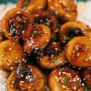 Sweet and sour mushrooms over a bowl of fluffy white rice, garnished with green onions and sesame seeds, ready to eat