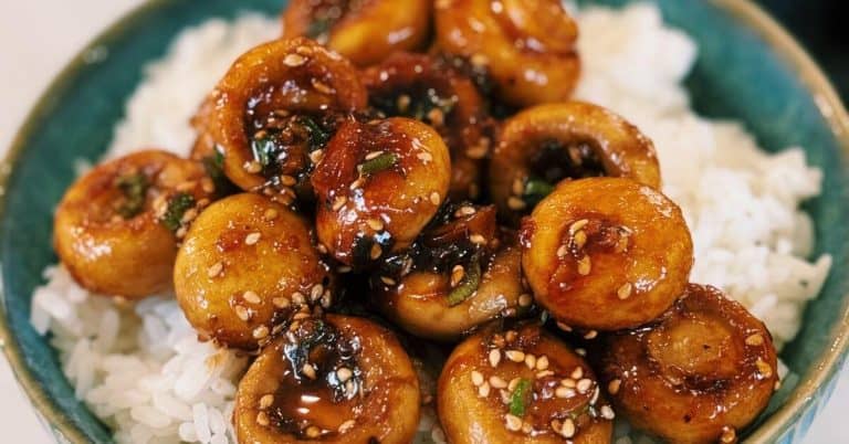 Sweet and sour mushrooms over a bowl of fluffy white rice, garnished with green onions and sesame seeds, ready to eat