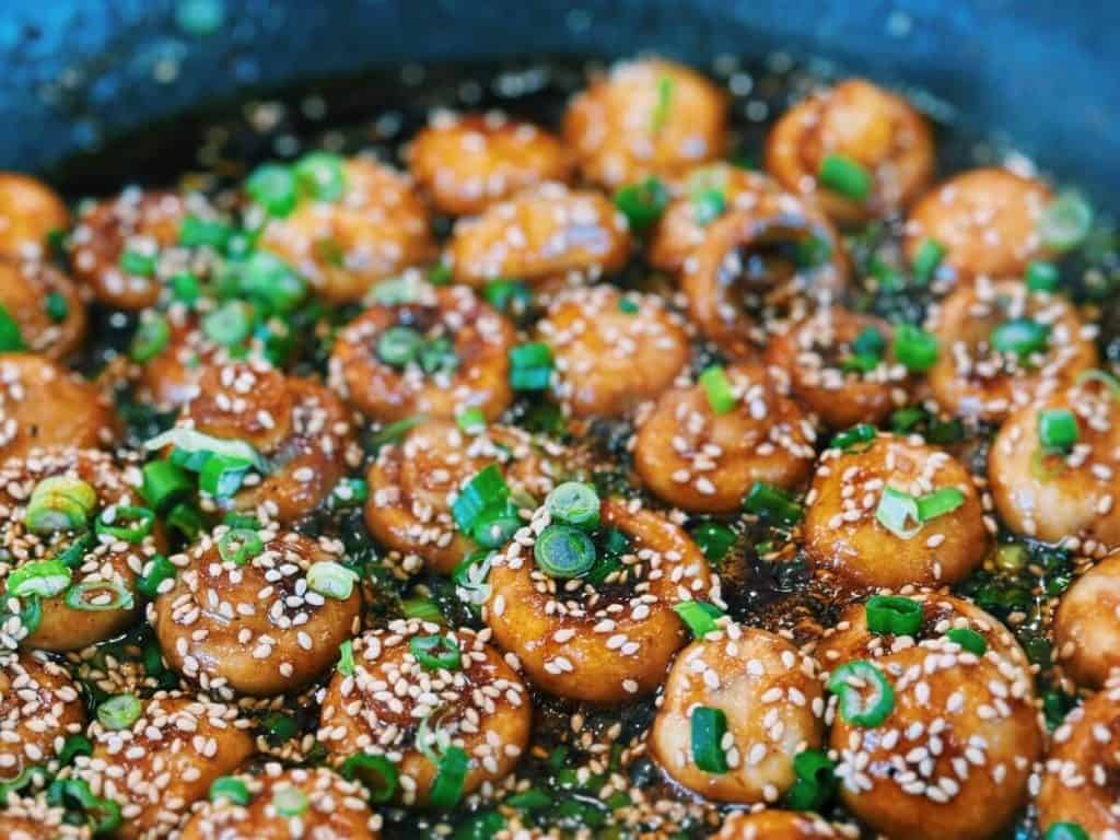 finished sweet and sour mushrooms garnished with green onions and sesame seeds in the pan ready to serve.