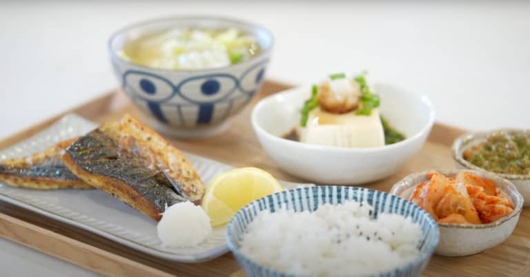 A full Japanese Traditional Breakfast containing air fried mackerel, tofu, miso soup, rice, natto and kimchi.