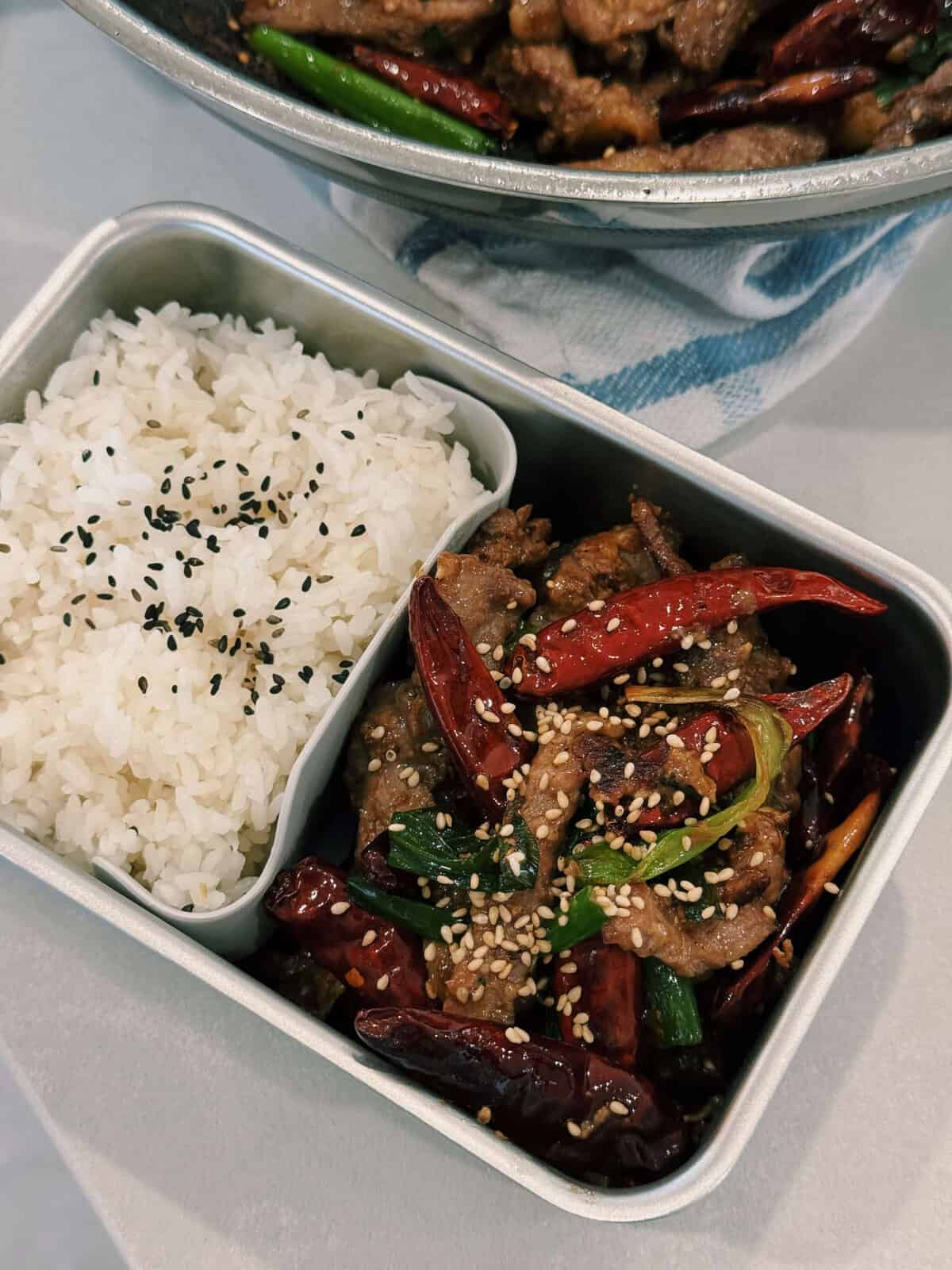 A showcase of hearty lunchboxes containing spicy scallion stir fry beef with a healthy helping of white rice topped with sesame seeds