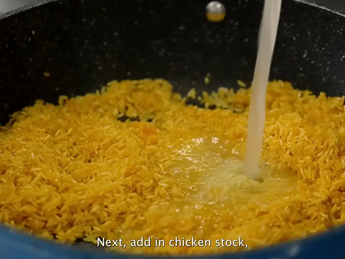 Adding broth into freshly toasted yellow turmeric rice