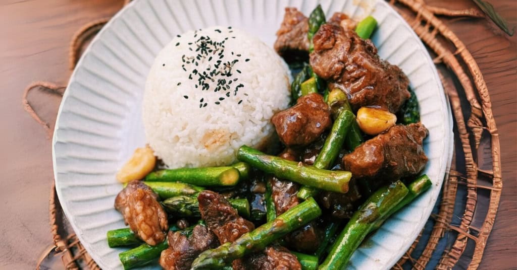 Stir Fry Asparagus Beef served on a white place with a bowl of rice. 