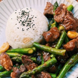 Stir Fry Asparagus Beef served on a white place with a bowl of rice.