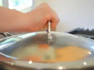 Making Ham and Cheese Breakfast Sandwich by laying cheese slices on cooked ham, and then covering the pan to make the cheese melt