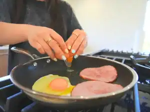 Making Ham and Cheese Breakfast Sandwich by first frying the ham slices and eggs in the same pan