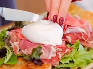 A close-up of the sandwich highlighting the contrast between the creamy burrata, pink pickled radishes, and green pesto on crusty bread.