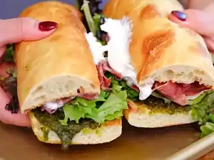 The completed sandwich cut in half, revealing the layers of burrata, prosciutto, pesto, and greens.