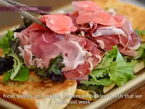 A step-by-step depiction of assembling the sandwich, showing pesto spread on toasted ciabatta, layered with prosciutto, pickled radishes, fresh greens, and topped with burrata.