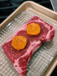 Gochujang Butter on top of raw steak on a baking sheet for Reverse Searing