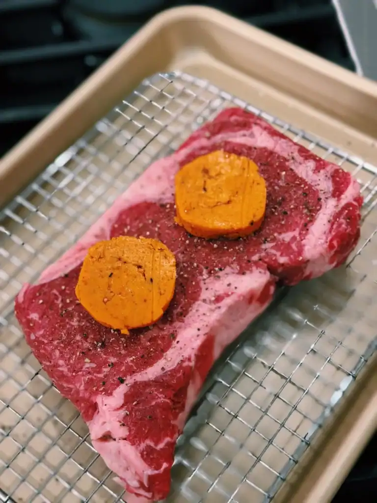 Gochujang Butter on top of raw steak on a baking sheet for Reverse Searing