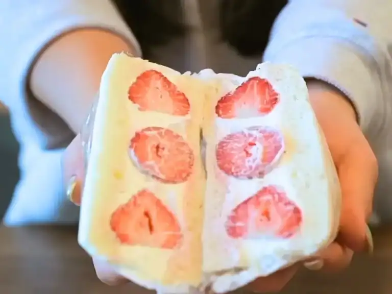 Japanese Fruit Sando cut diagonally in half, showing 3 halved strawberries sandwiched in between Japanese milk bread and fresh homemade whipped cream