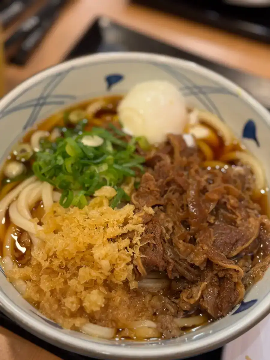 A bowl of beef udon with soft boiled egg and tempura bits at Marugame Udon in Waikiki, Honolulu, Hawaii