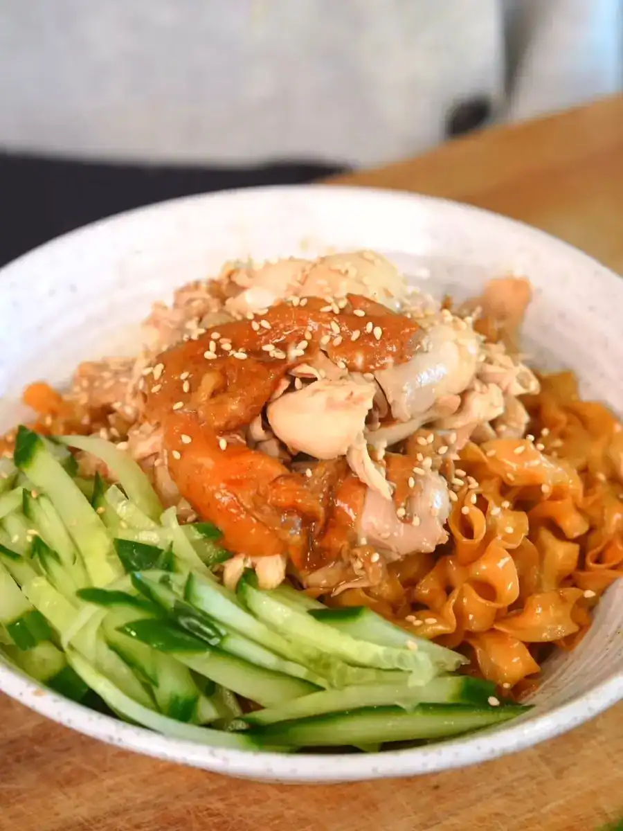 A bowl of braised scallion soy chicken noodles garnished with shredded cucumbers and chicken