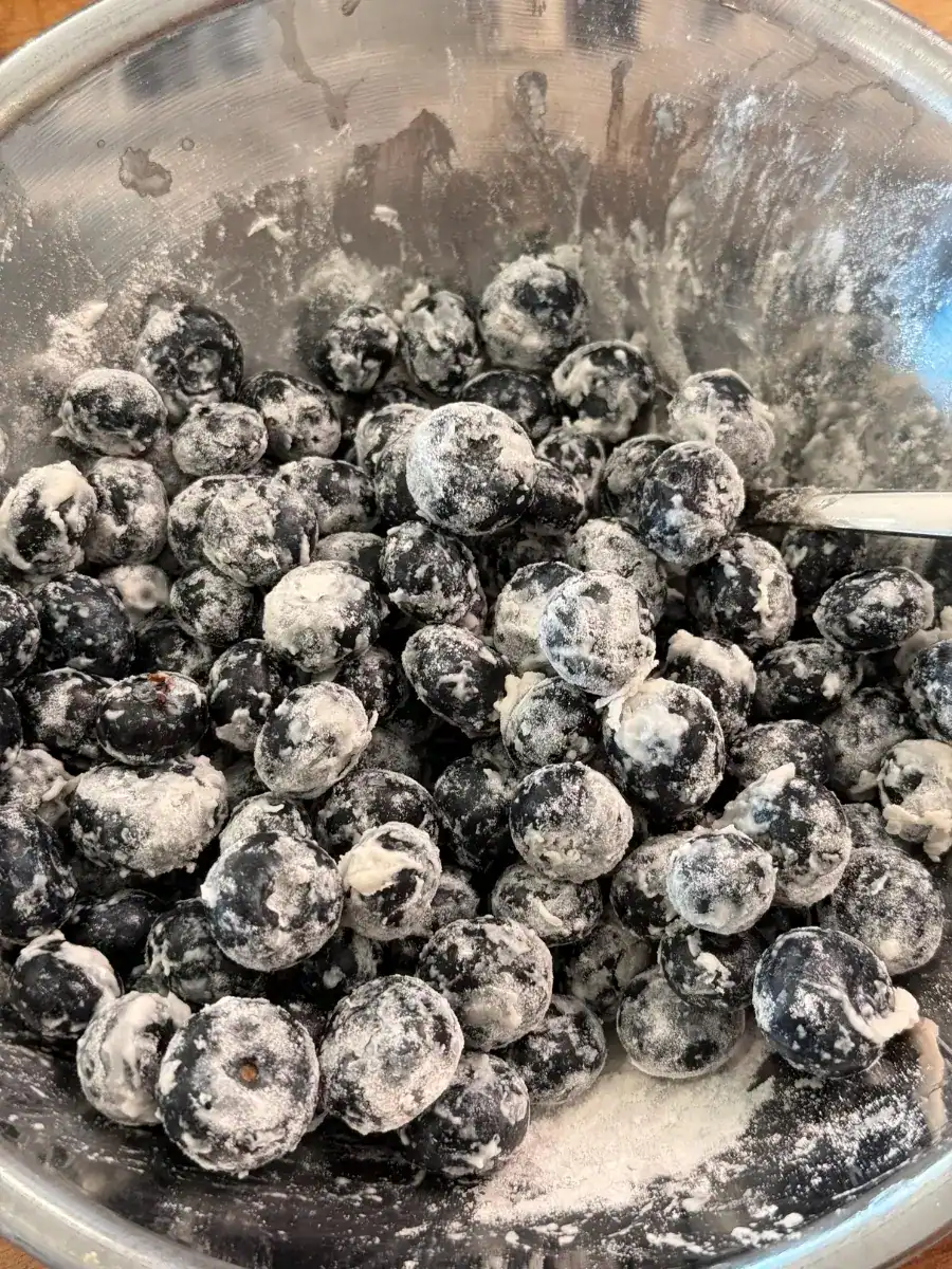 Dusting blueberries with flour for lemon blueberry loaf. This ensures that the blueberries don’t sink to the bottom
