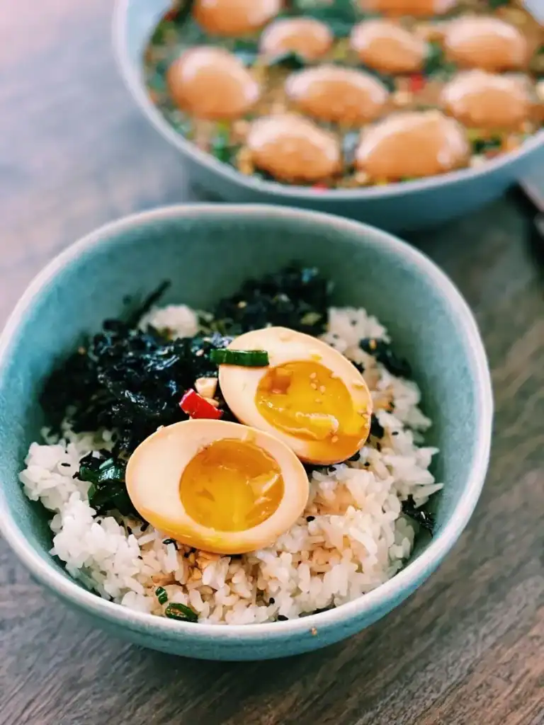 Mayak Gyeran or Soy Marinated Korean Eggs with jammy yolk halved, served over rice drizzled with Marinade and crispy seaweed