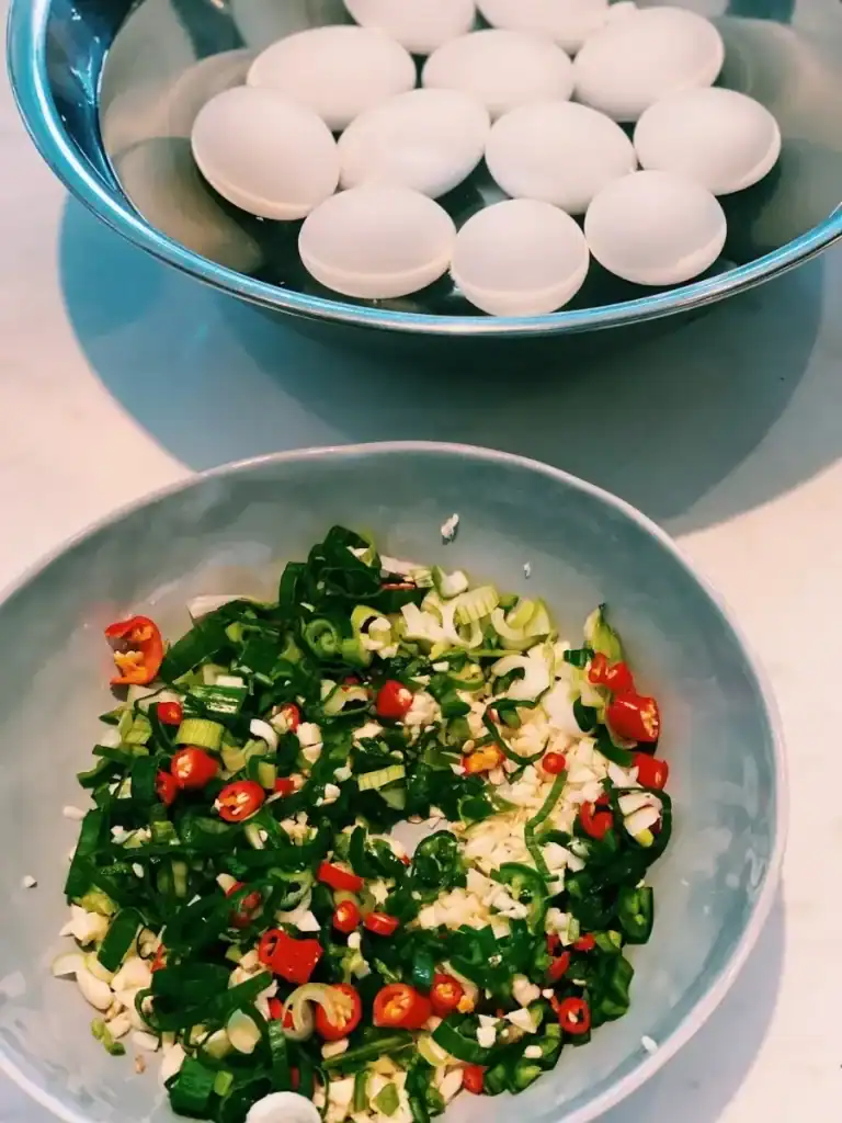 The chopped ingredients for Mayak Gyeran, or Korean Spicy Soy Eggs marinade, with a bowl of eggs in the background 