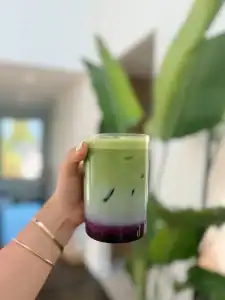 A glass of layered matcha, milk, and blueberry syrup for a yummy Blueberry Matcha Latte