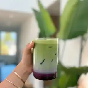 A glass of layered matcha, milk, and blueberry syrup for a yummy Blueberry Matcha Latte